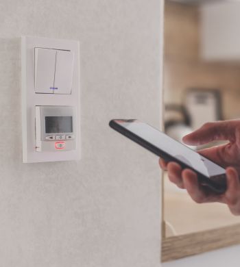 Smartphone connecting to floor heating controller in kitchen. Remote home control system on a smartphone